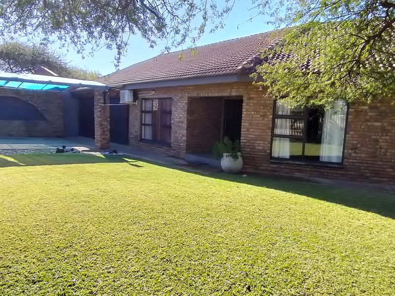 A well-maintained rear exterior view of a face brick house featuring a covered patio area and a neat, established lawn.
