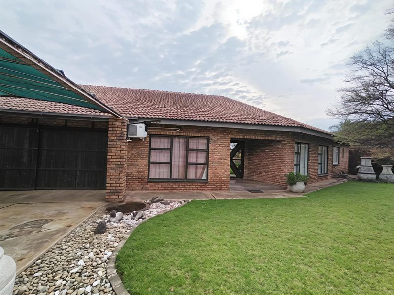 Front view of a single-story brick house featuring a tiled roof, attached garage, carport, and a well-maintained lawn with stone landscaping.