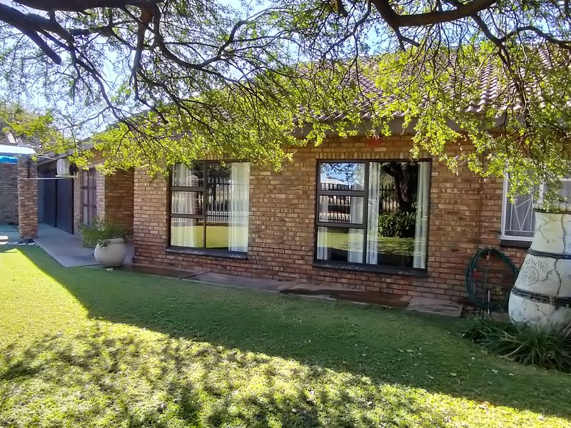 Rear view of a brick house featuring a well-maintained lawn, aluminium windows, and a swimming pool area with a cover.