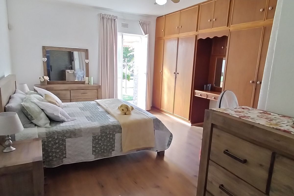 A spacious bedroom featuring extensive built-in wooden cabinetry, laminate flooring, and direct access to an outdoor patio area.