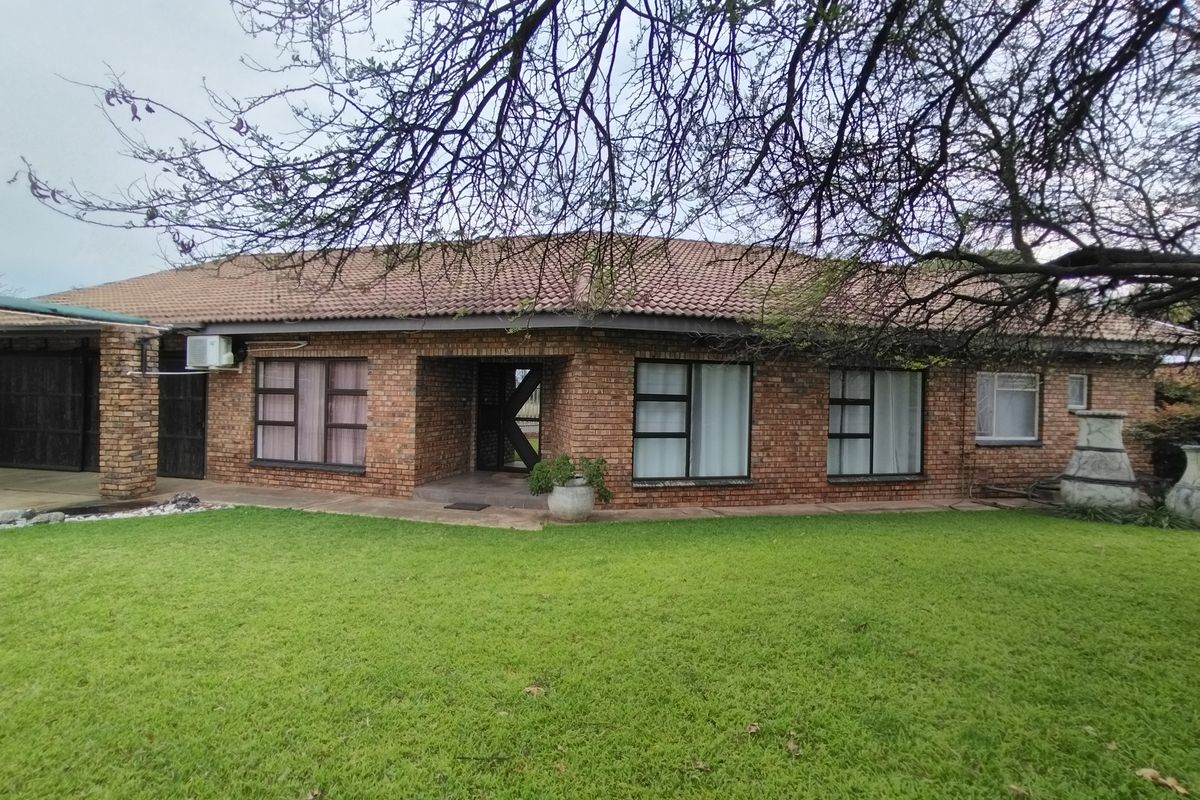 A rear view of a face-brick house featuring a tiled roof, aluminium window frames, and a built-in outdoor braai area overlooking a lawn.