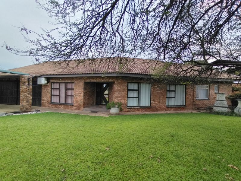 A rear view of a face-brick house featuring a tiled roof, aluminium window frames, and a built-in outdoor braai area overlooking a lawn.