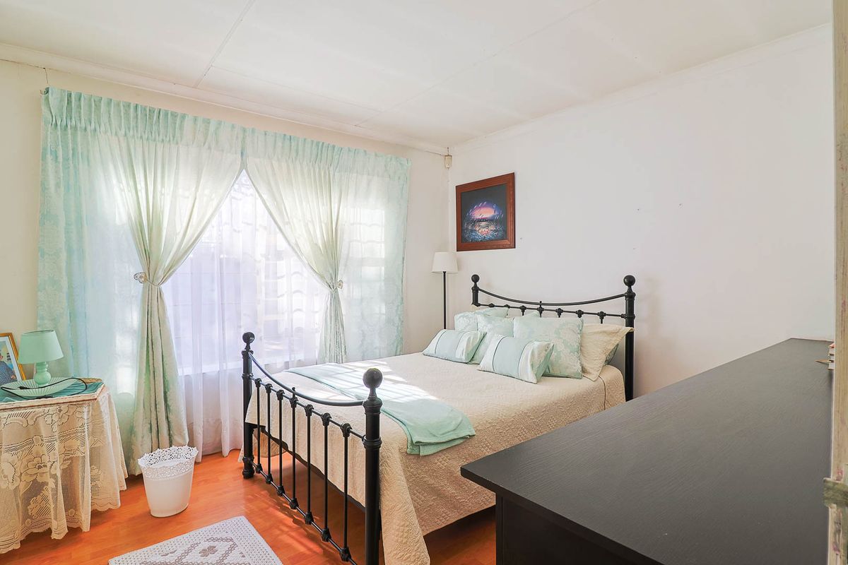 A standard bedroom featuring laminate flooring and large windows with curtain treatments, offering a neutral base for potential interior updates.