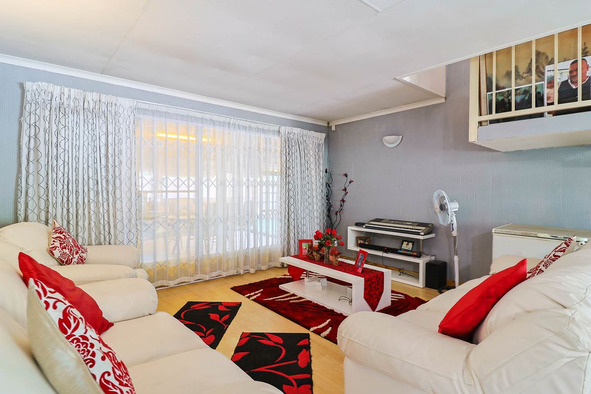 A living room featuring laminate flooring, coved ceilings, and a sliding glass door with security gate leading to an outdoor area.