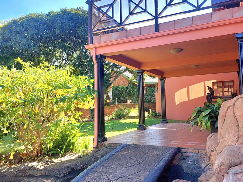 A covered ground-floor patio area featuring tiled flooring and decorative columns, leading out to a landscaped garden with a stone pathway.