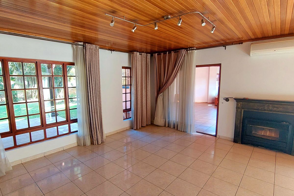 Spacious living room featuring a warm timber-clad ceiling, ceramic tiled flooring, a built-in fireplace, and large timber-framed windows overlooking the garden.
