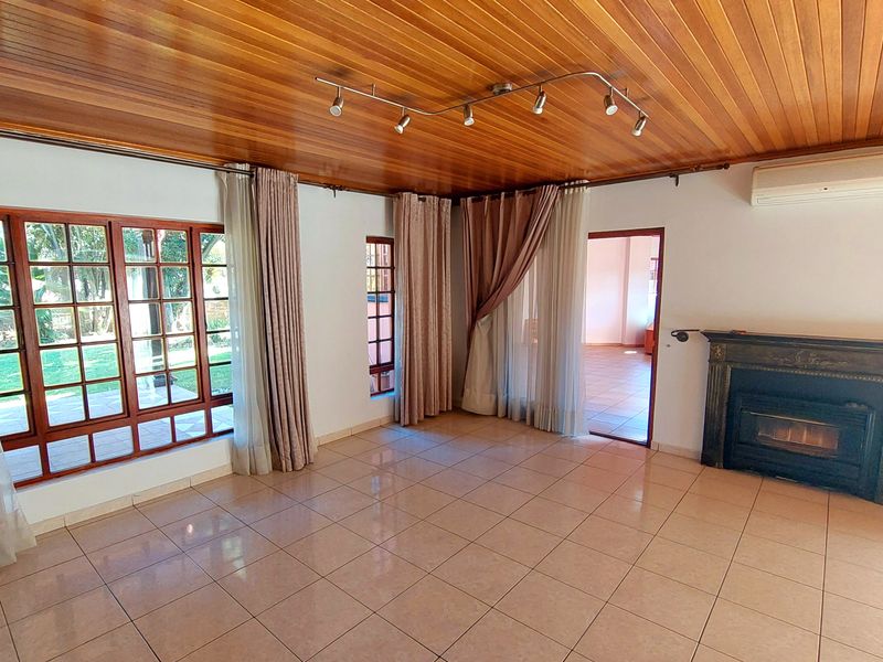 Spacious living room featuring a warm timber-clad ceiling, ceramic tiled flooring, a built-in fireplace, and large timber-framed windows overlooking the garden.