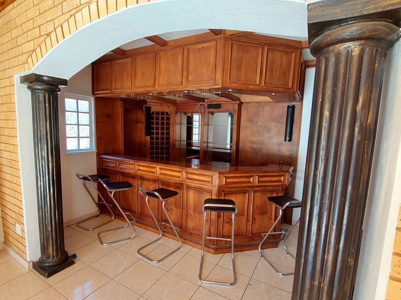 A dedicated home bar area featuring custom built-in wooden cabinetry, a brick archway with decorative columns, and tiled flooring.