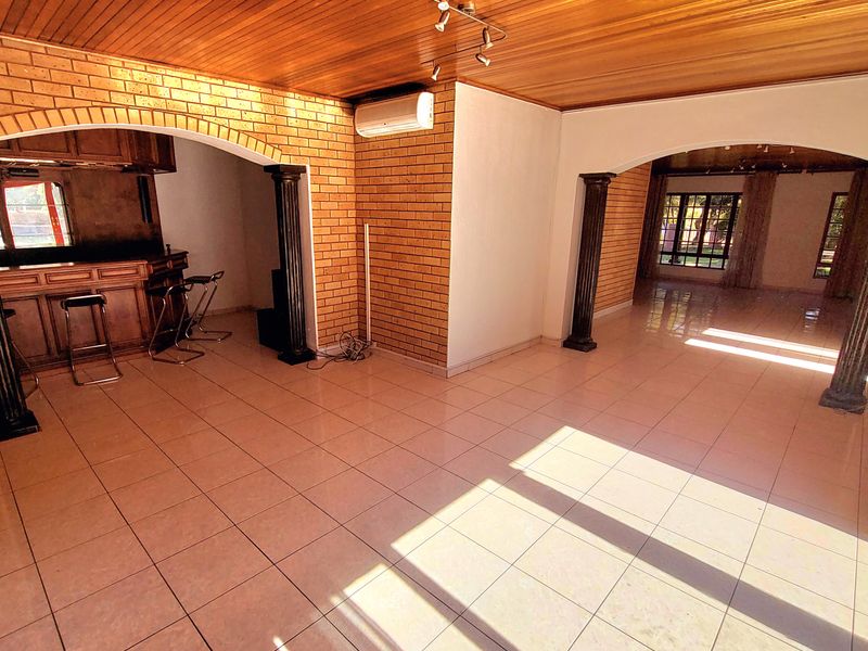 Spacious open-plan living area featuring timber ceilings, exposed brick walls, ceramic tiling, and a built-in bar area with decorative archways and columns.