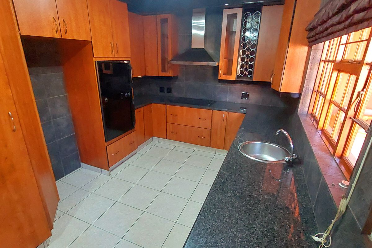 A functional kitchen featuring wooden cabinetry, granite countertops, a built-in oven, extractor fan, and tiled flooring with a neutral backsplash.