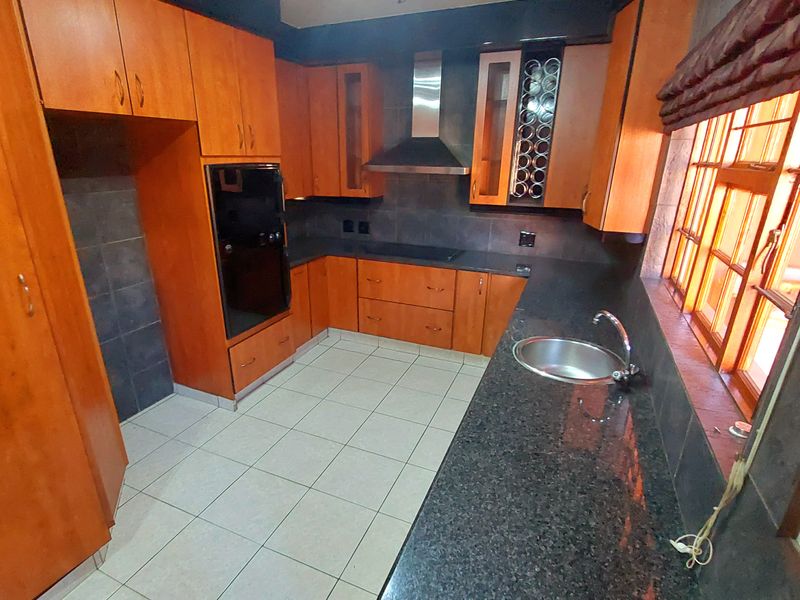 A functional kitchen featuring wooden cabinetry, granite countertops, a built-in oven, extractor fan, and tiled flooring with a neutral backsplash.