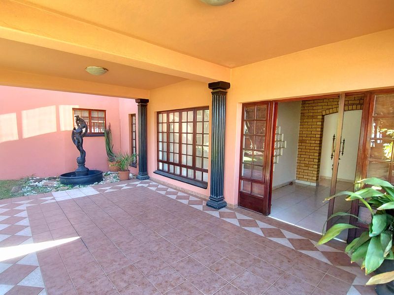 A covered patio area featuring tiled flooring, decorative columns, and direct access to the interior through wooden framed doors.