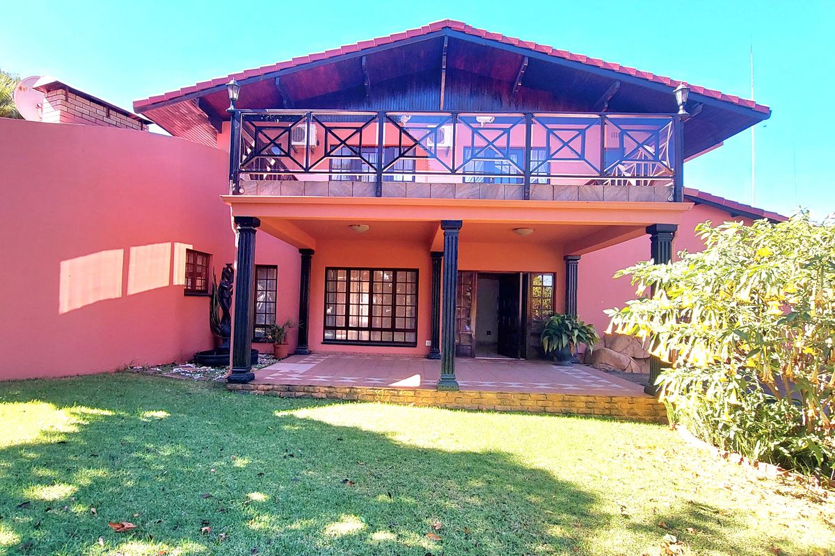 Rear view of the property featuring a covered patio, an upper-level balcony with decorative railing, and a well-maintained garden area.