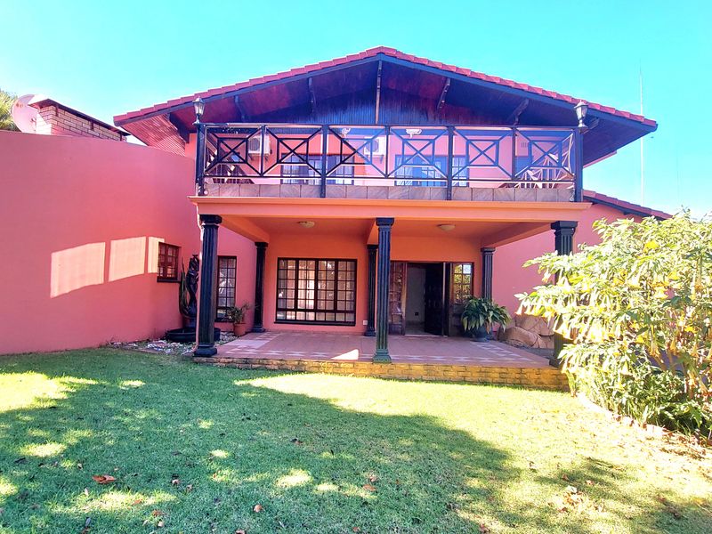 Rear view of the property featuring a covered patio, an upper-level balcony with decorative railing, and a well-maintained garden area.