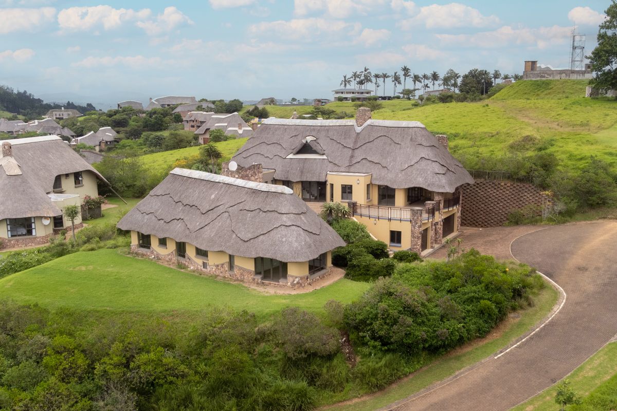 Aerial view of a large thatched-roof residence featuring stone cladding, a balcony, and a paved driveway set within a landscaped estate.