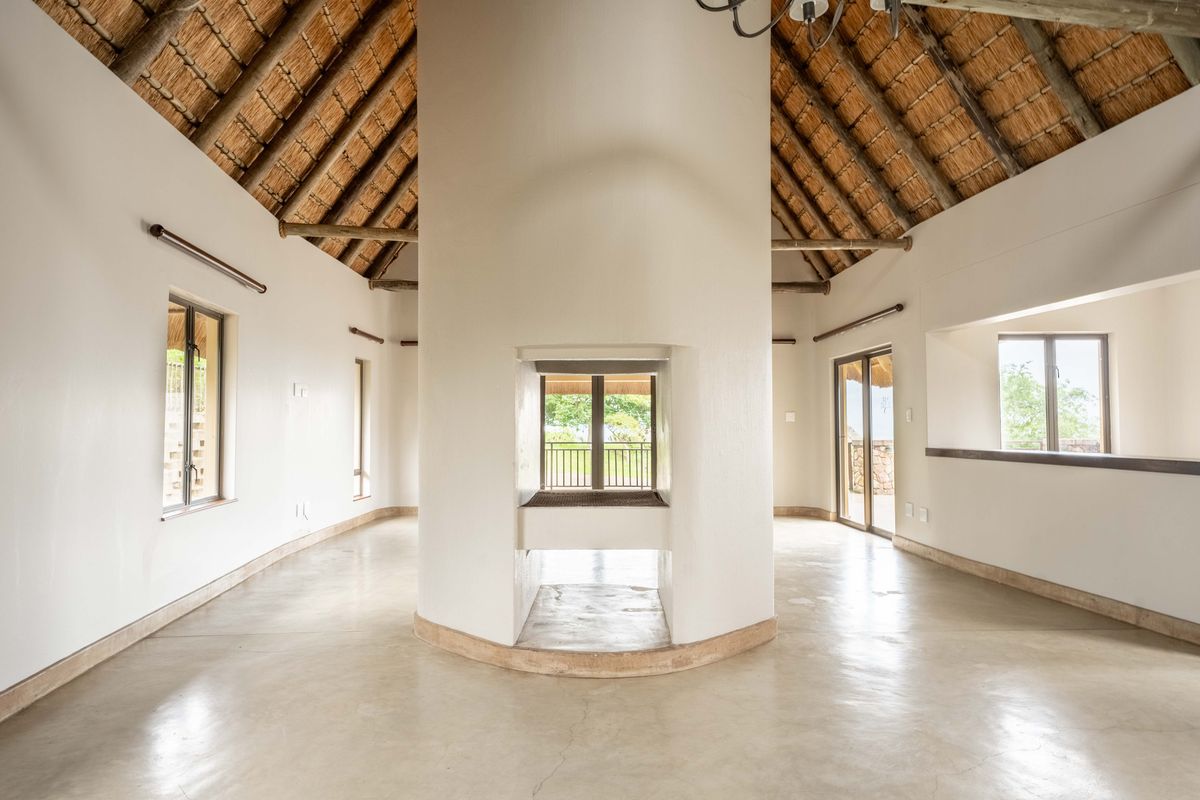 Spacious living area featuring a unique central masonry fireplace, high vaulted thatched ceiling with exposed rafters, and polished concrete floors with abundant natural light.