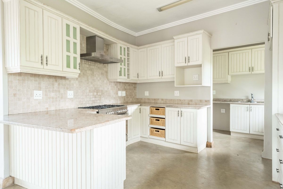 Spacious kitchen featuring white cabinetry, stone countertops, a gas hob with extractor, and an adjoining scullery area with additional storage and sink.