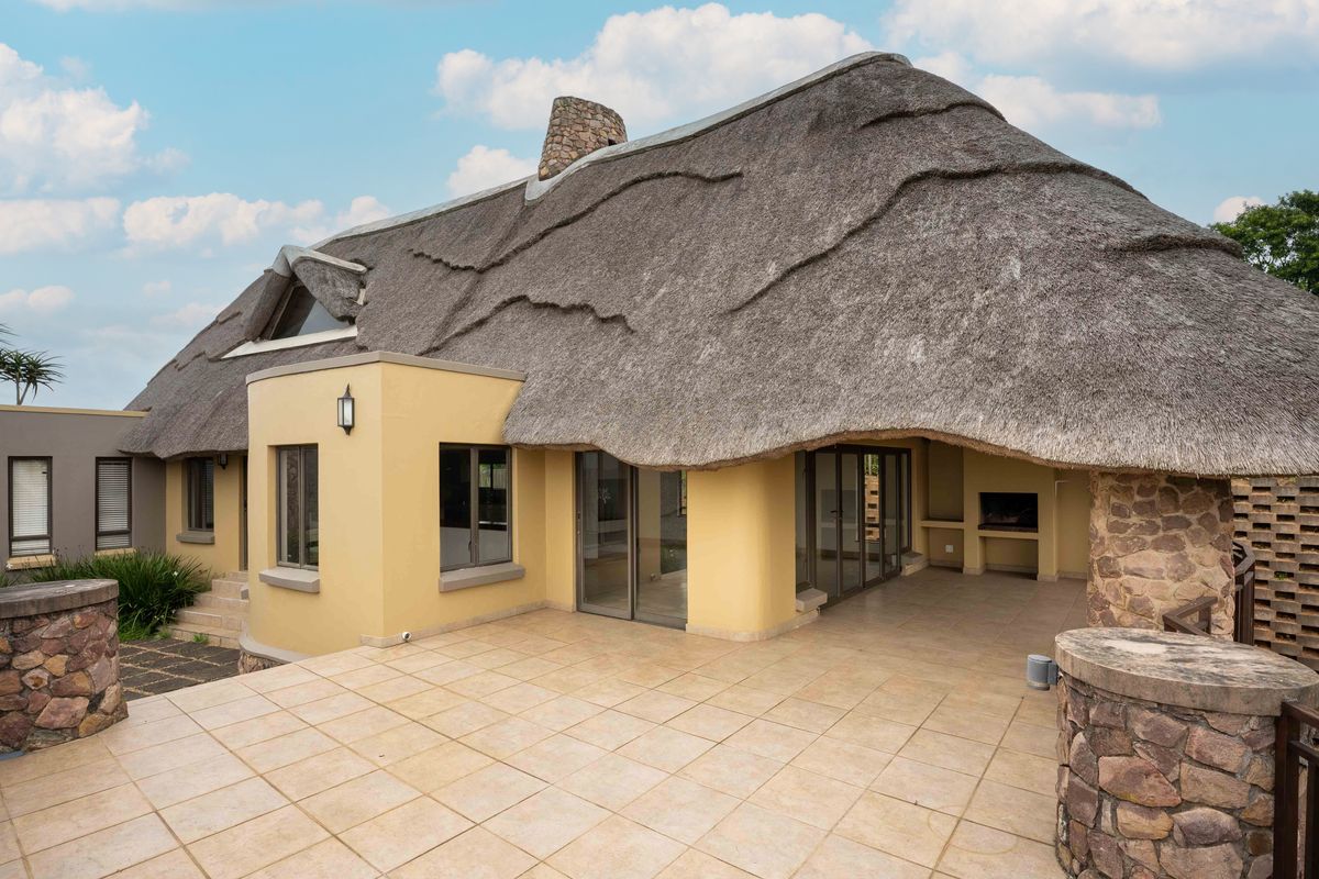 Spacious rear patio featuring a large thatched roof, stone accents, and a built-in braai area, perfect for outdoor entertaining.