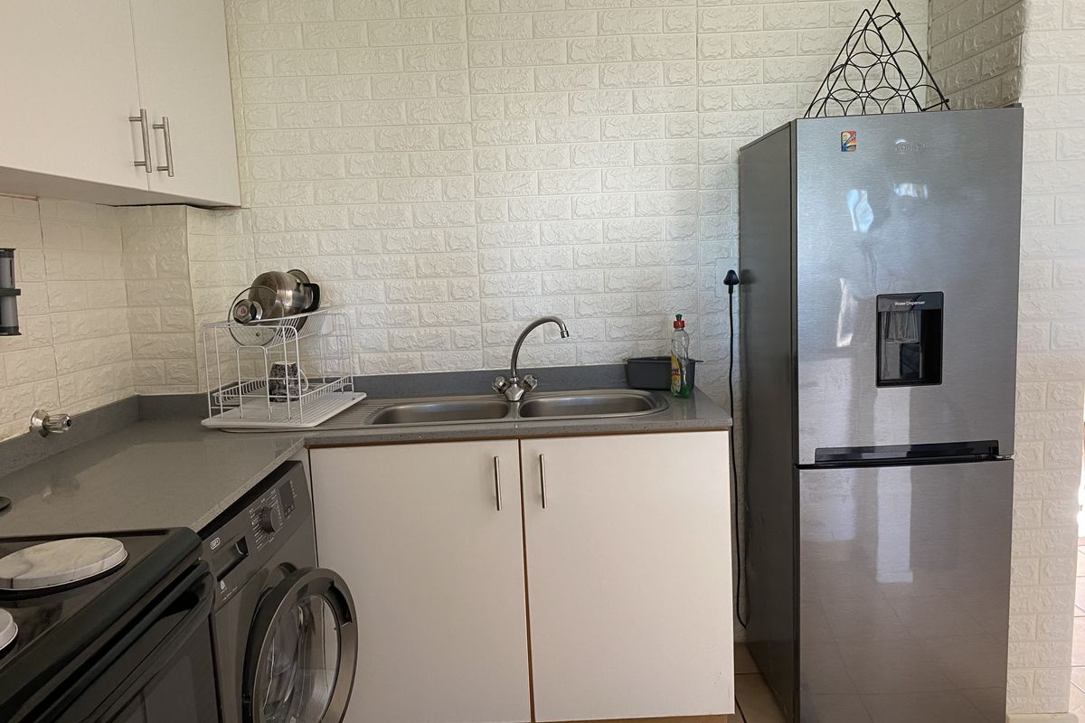 Compact kitchen area featuring built-in cabinetry, a double basin sink with mixer tap, and textured wall cladding.