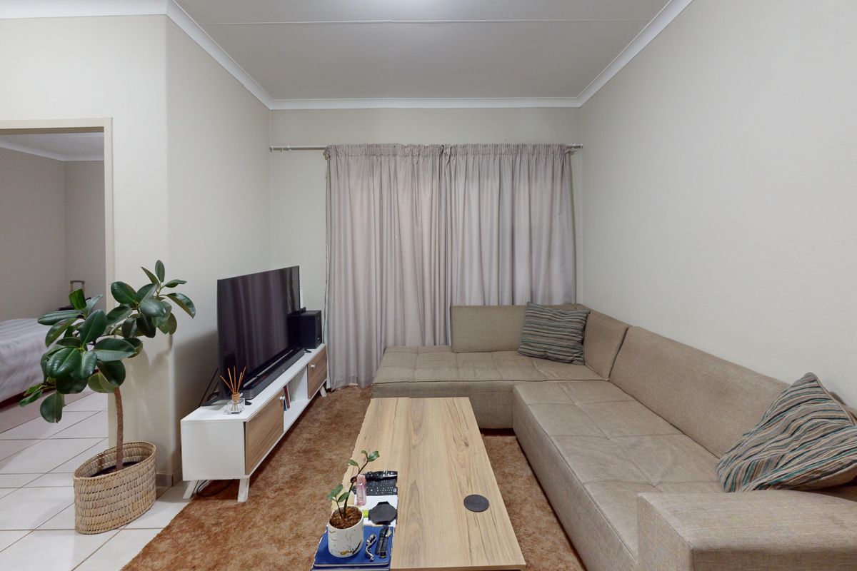 A well-maintained living room featuring neutral wall tones, cove cornicing, and a functional layout with access to an adjacent bedroom area.