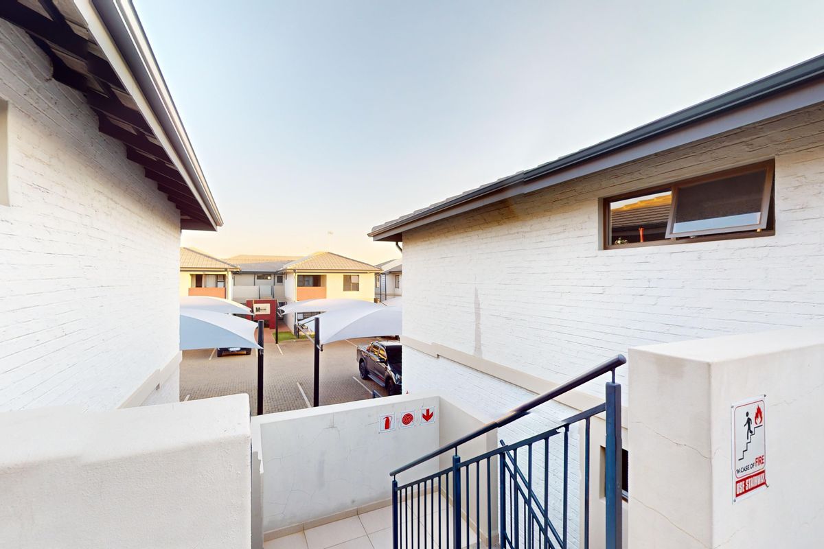 Exterior view of a townhouse complex featuring a metal staircase, painted brick walls, and covered parking bays in the background.