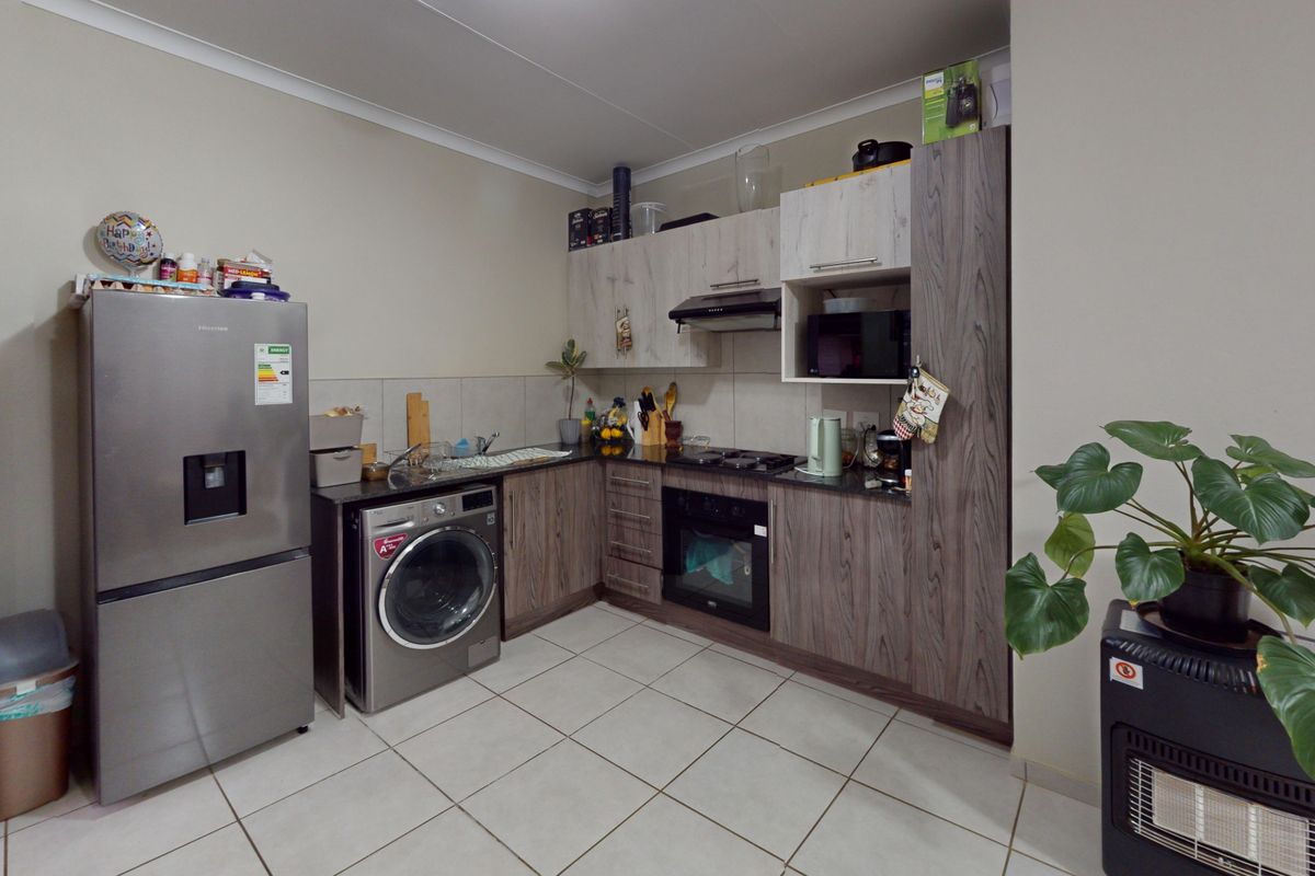 A functional kitchen featuring wood-grain cabinetry, dark countertops, built-in oven with gas hob, extractor fan, and tiled flooring.