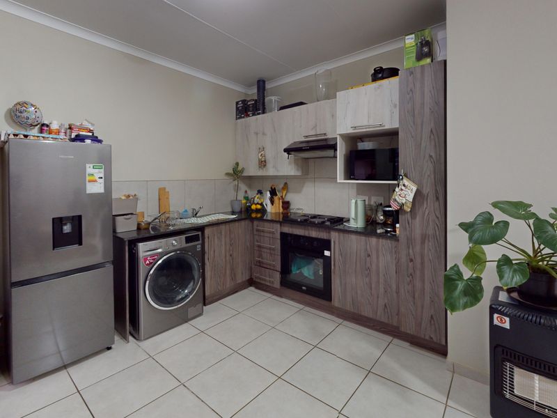 A functional kitchen featuring wood-grain cabinetry, dark countertops, built-in oven with gas hob, extractor fan, and tiled flooring.