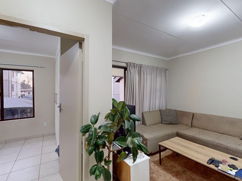 A living room area featuring tiled flooring, neutral wall finishes, and access to an adjacent room with built-in storage.