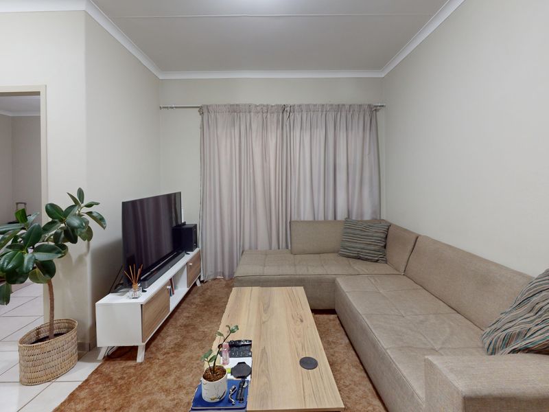 A well-maintained living room featuring neutral wall tones, cove cornicing, and a functional layout with access to an adjacent bedroom area.