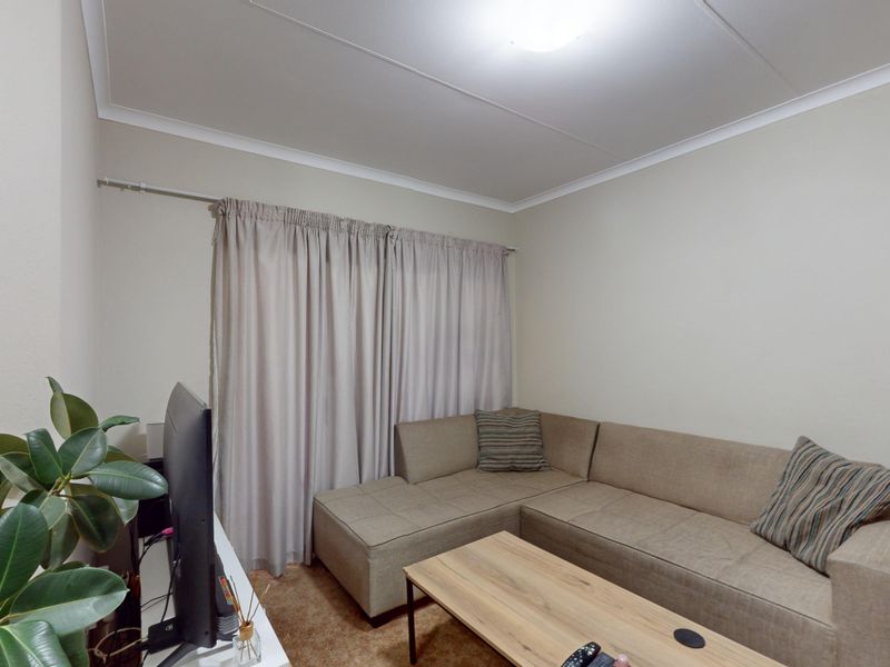 A compact living room featuring neutral wall finishes, cove cornicing, and a window fitted with a curtain rod.