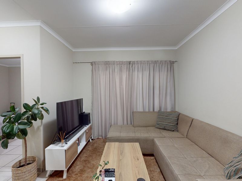 A neutrally painted living room featuring cove cornicing and skirting boards, with a view into an adjacent bedroom area.