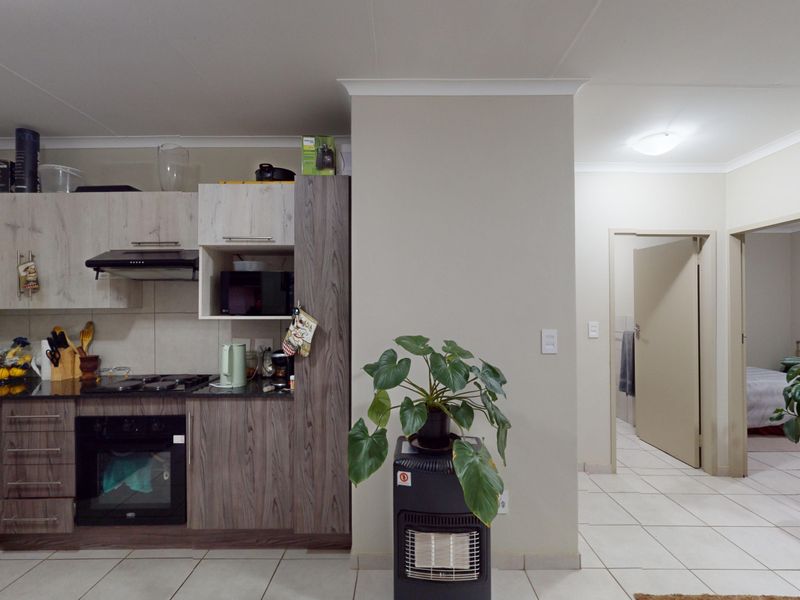 Open-plan kitchen featuring modern wood-grain cabinetry, granite countertops, and integrated appliances, flowing into a tiled hallway leading to adjacent rooms.