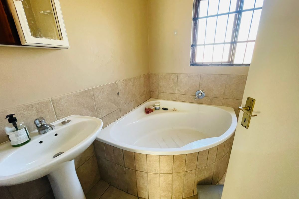 A functional bathroom featuring a corner bathtub, pedestal basin, and tiled splashbacks, illuminated by natural light from a window with security bars.