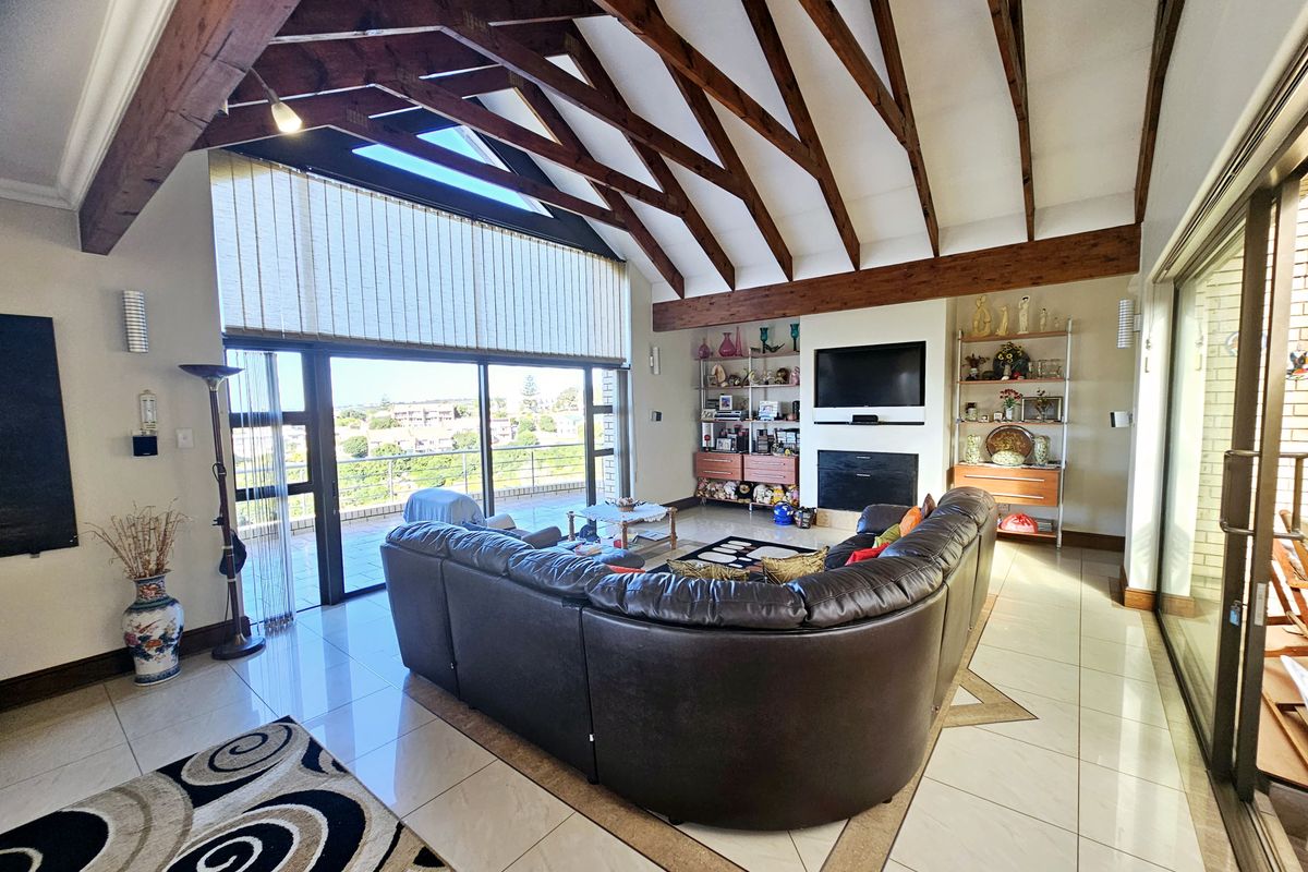 Spacious living room featuring a vaulted ceiling with exposed timber rafters, a built-in fireplace, tiled flooring, and large sliding doors opening to a balcony.