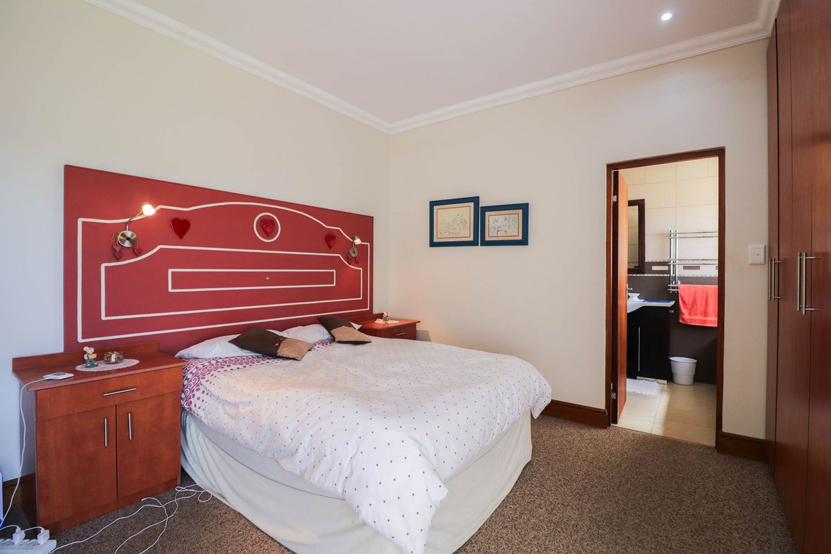 A carpeted bedroom featuring built-in cupboards and direct access to an en-suite bathroom with tiled finishes.