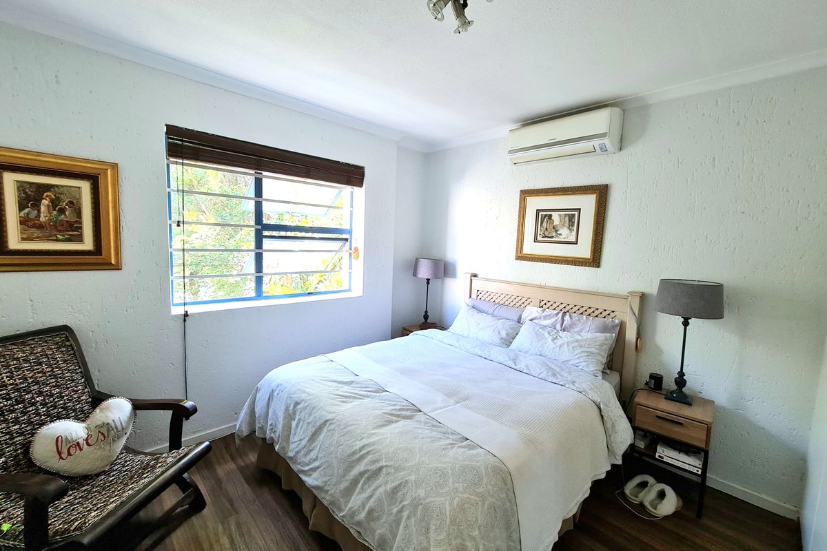 A cozy bedroom featuring laminate flooring, a split-system air conditioner, and a louvered window with security bars.