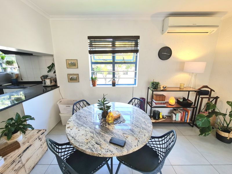 An open-plan living and kitchen area featuring tiled flooring, a granite countertop, and a wall-mounted air conditioning unit.