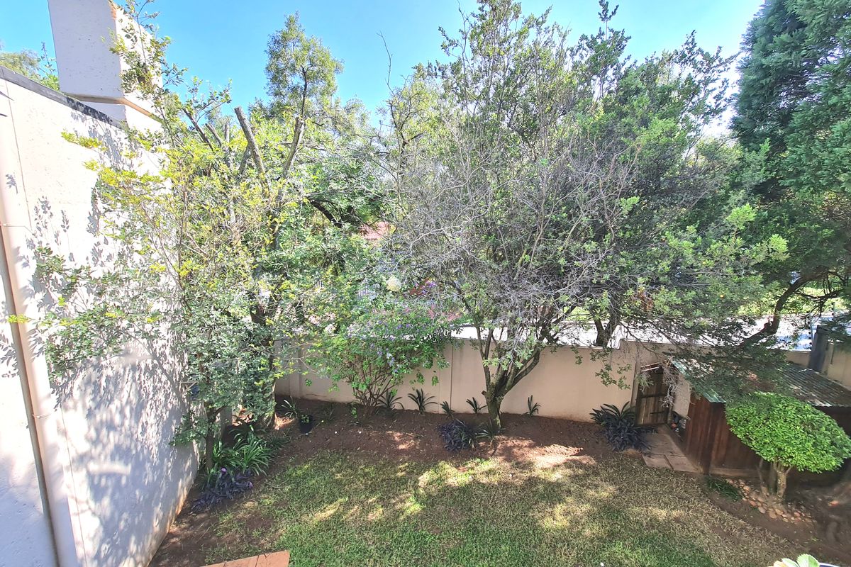 A private rear garden area featuring a lawn, mature trees, a boundary wall, and a small storage shed.