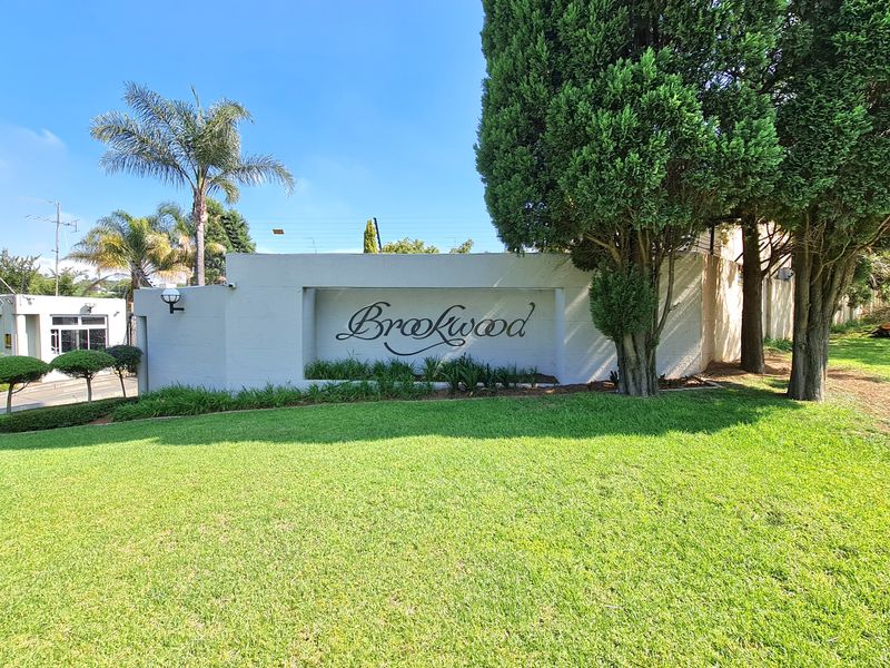 The entrance to Brookwood apartment complex featuring a prominent signage wall, well-maintained lawn, and mature landscaping.