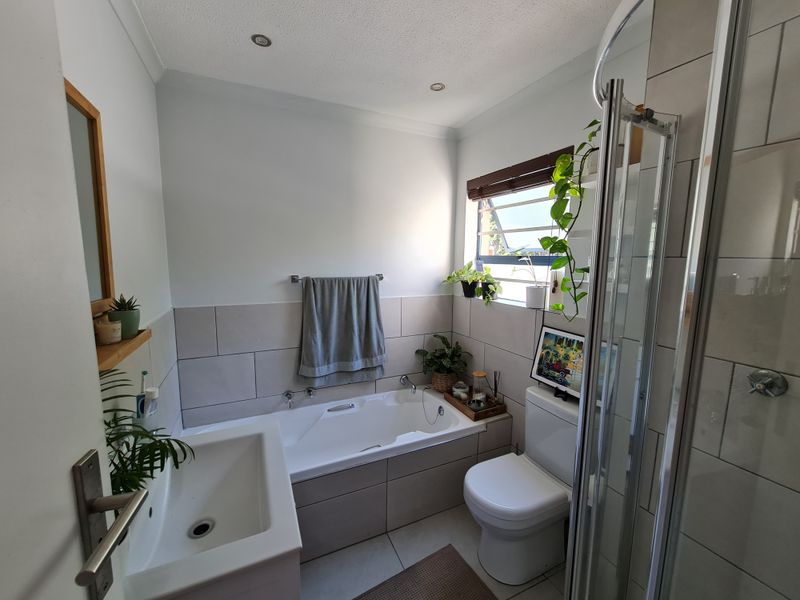 A well-maintained bathroom featuring a built-in bathtub, separate shower enclosure, toilet, and vanity basin with neutral wall and floor tiling.