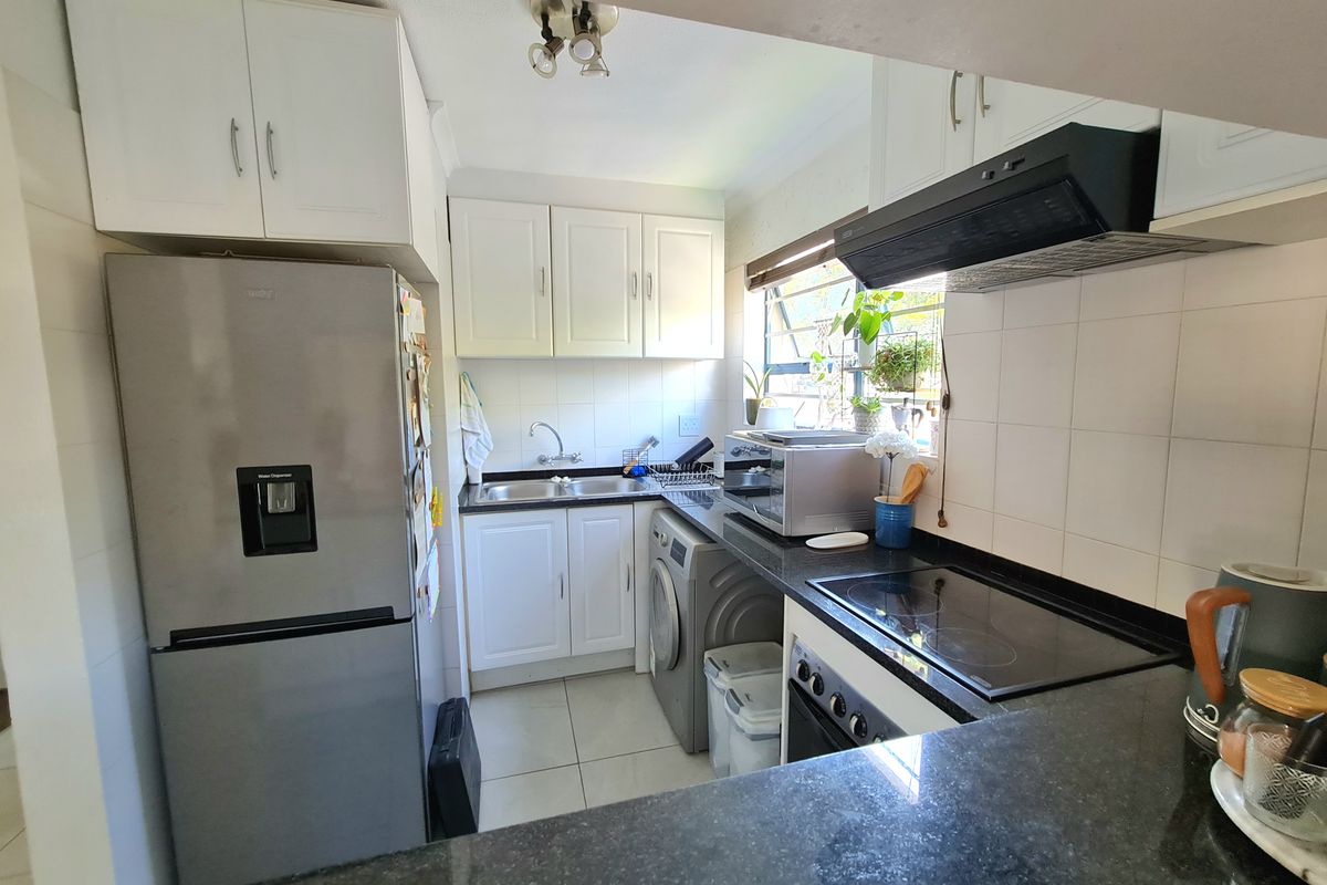 A functional kitchen featuring white cabinetry, dark granite countertops, integrated appliances, and tiled finishes, offering a practical layout for daily use.