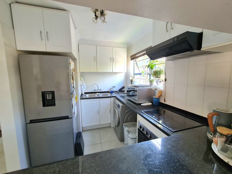 A functional kitchen featuring white cabinetry, dark granite countertops, integrated appliances, and tiled finishes, offering a practical layout for daily use.