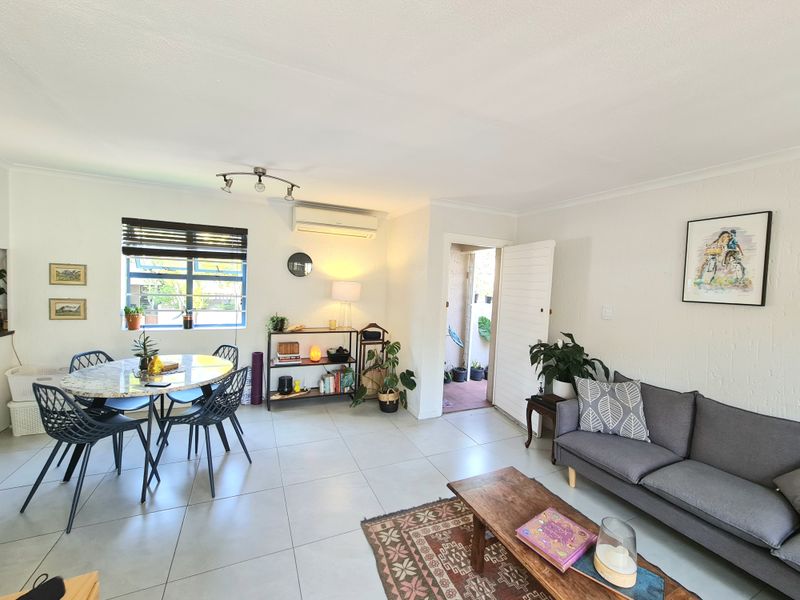 Bright open-plan living and dining area featuring neutral tiled flooring, an air conditioning unit, and direct access to an outdoor space.