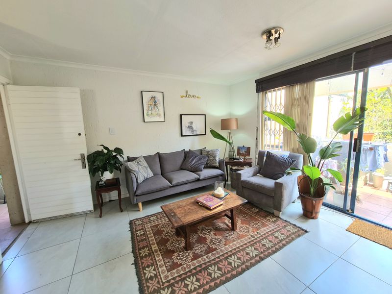 A bright living room featuring tiled flooring, a sliding glass door with security gate, and direct access to an outdoor patio area.