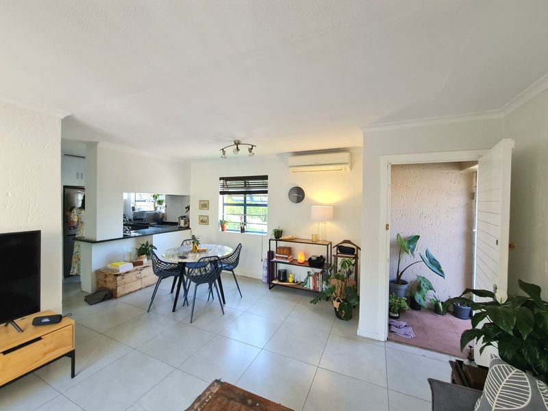 An open-plan living and dining area featuring tiled floors, a split-system air conditioner, and a functional kitchen pass-through window.
