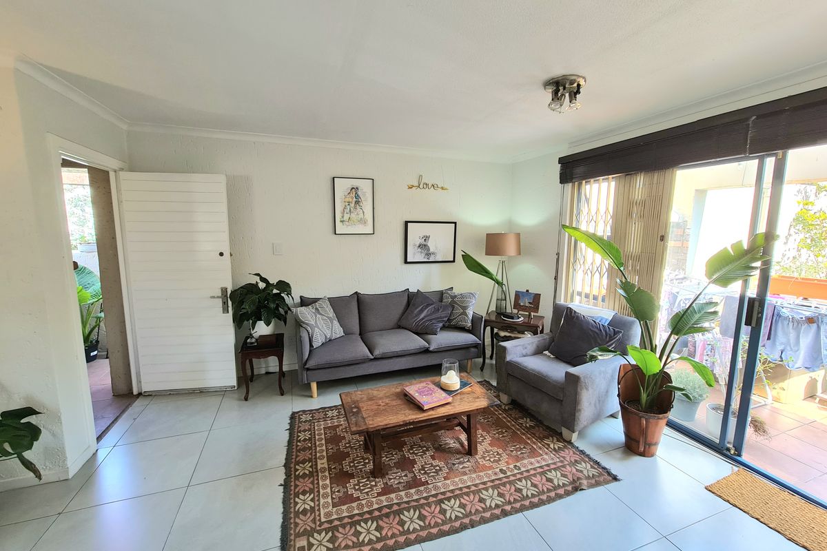 A bright living room featuring large format floor tiles and a sliding glass door providing access to an outdoor patio area.
