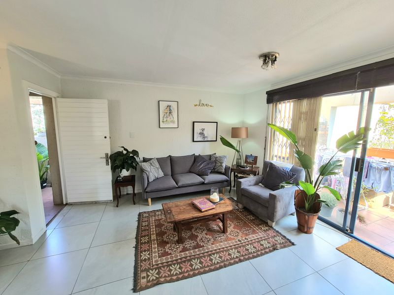 A bright living room featuring large format floor tiles and a sliding glass door providing access to an outdoor patio area.