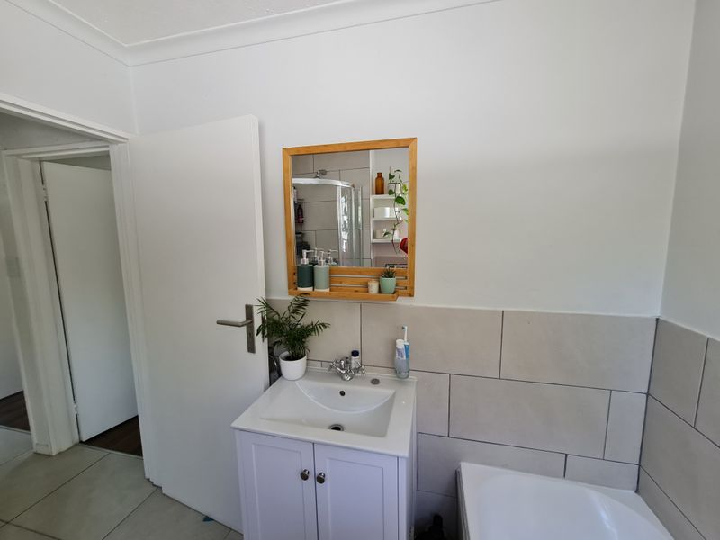 A clean bathroom featuring a modern vanity cabinet with a ceramic basin, chrome mixer tap, wall-mounted mirror, and tiled splashback.
