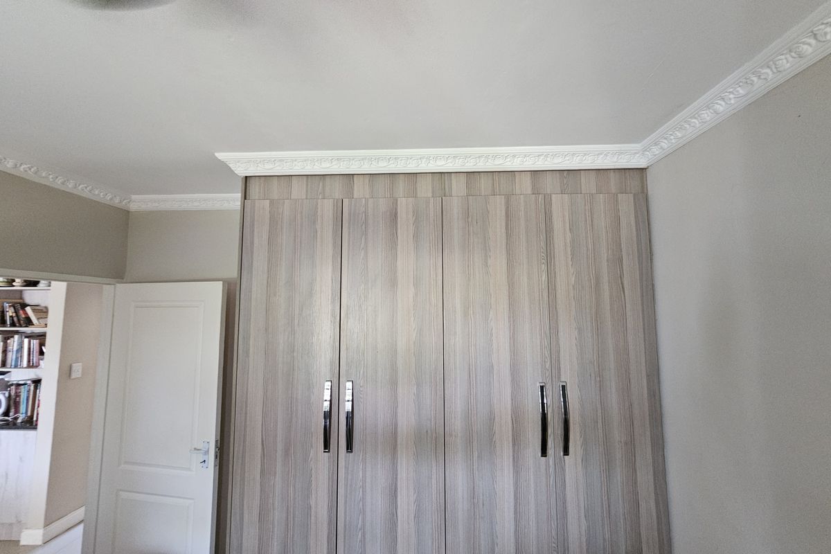 A bedroom featuring modern wood-grain built-in wardrobes with sleek handles and decorative ceiling cornicing.