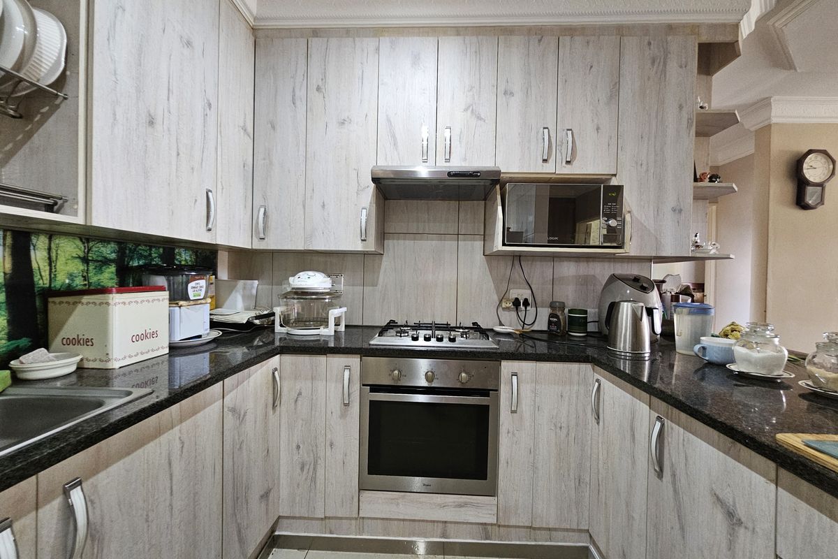 A functional kitchen featuring light wood-grain cabinetry, granite countertops, a gas hob, built-in oven, and integrated microwave with tiled flooring.